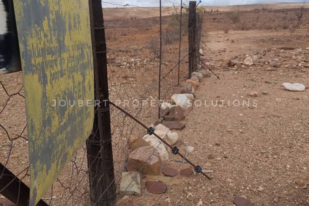 A view of the farm boundary featuring weathered wire fencing, wooden posts, and arid landscape terrain.