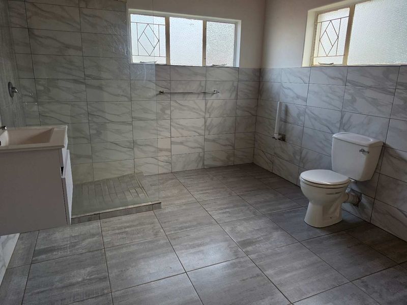A modern, tiled bathroom featuring a walk-in shower with a glass screen, a vanity basin, and a toilet.