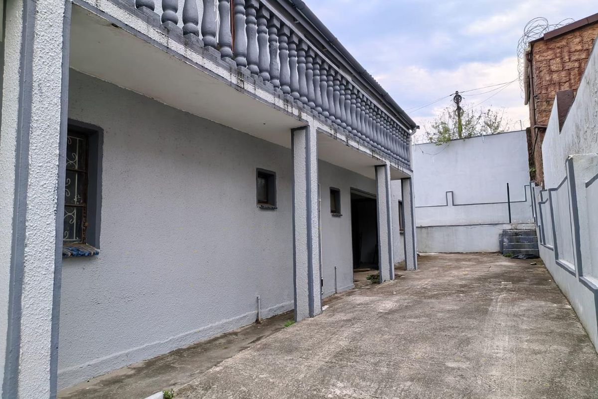 Rear exterior view of the property featuring a concrete driveway, a covered balcony with balustrades, and perimeter walling.