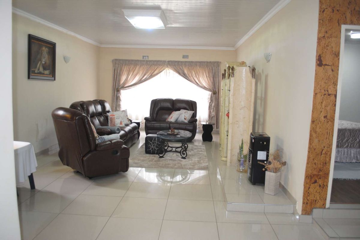 Spacious living room featuring large format floor tiles, recessed ceiling lighting, and a raised platform area, providing a comfortable and functional living space.