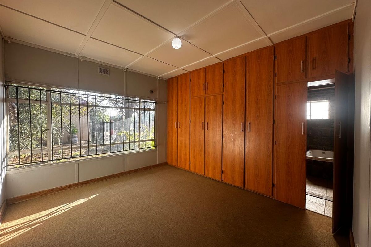 A bedroom featuring extensive built-in wooden cabinetry, large windows with security bars, and an adjoining bathroom.