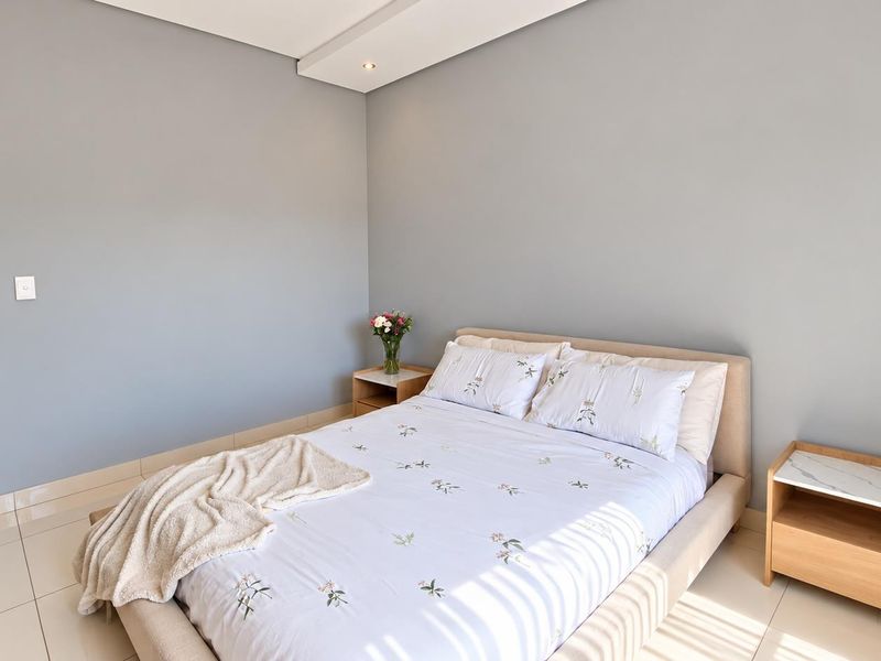 A well-maintained bedroom featuring neutral grey walls, tiled flooring, and recessed ceiling lighting, with an adjoining view into the bathroom.