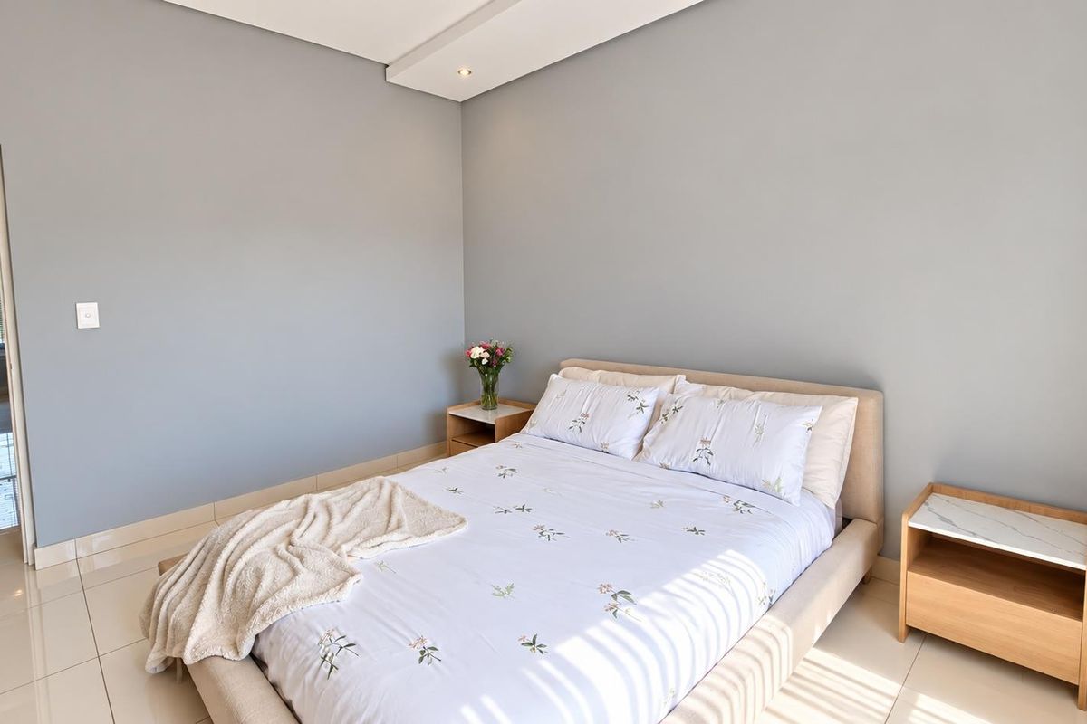 A well-maintained bedroom featuring neutral grey walls, tiled flooring, and recessed ceiling lighting, with an adjoining view into the bathroom.