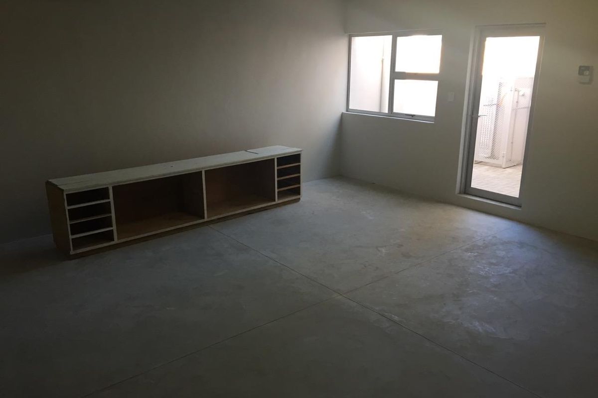 An unfinished interior space featuring concrete flooring, a built-in storage unit, and direct access to an outdoor area through a glass door.