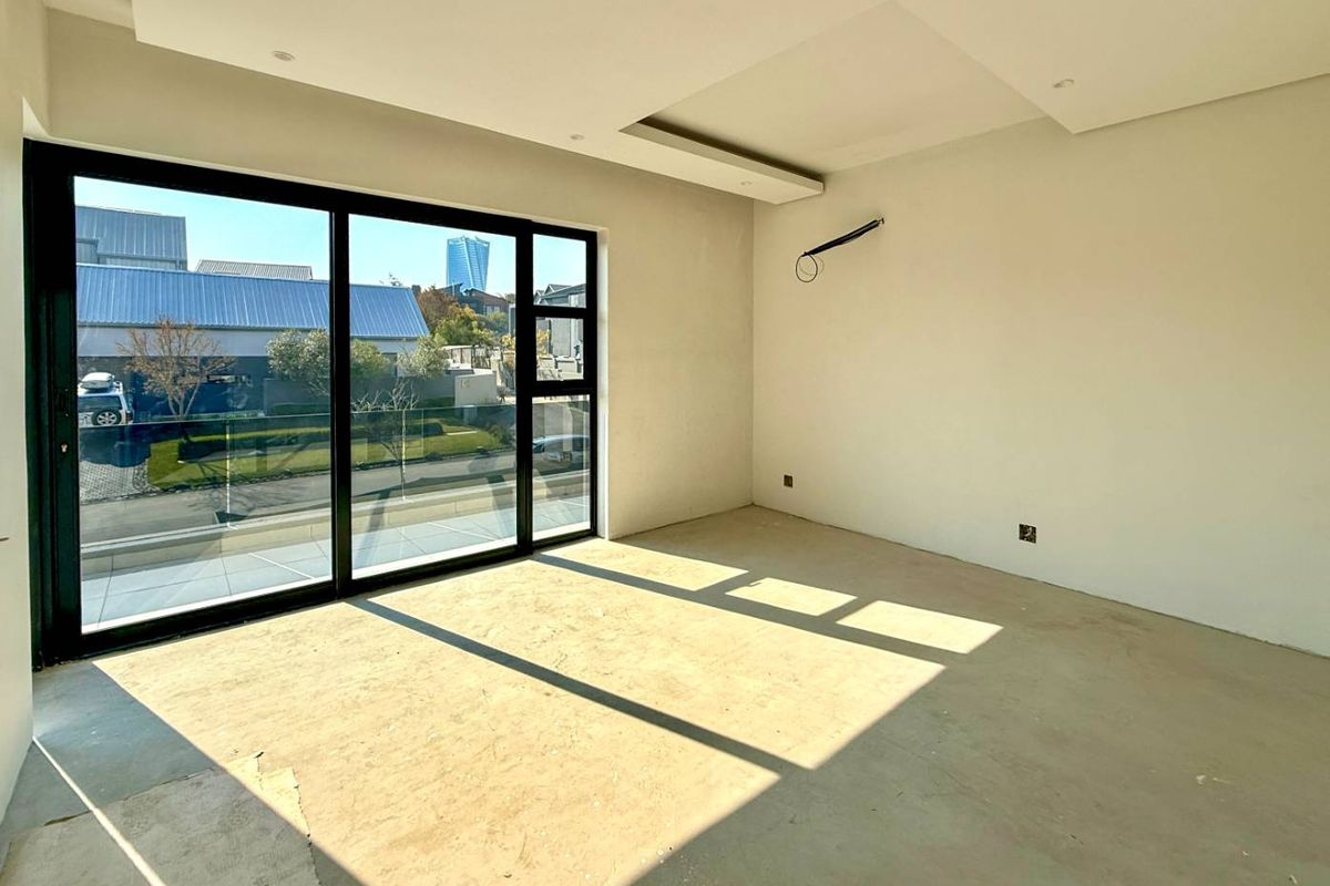 An empty, unfinished bedroom featuring recessed ceiling lighting, large sliding glass doors leading to a balcony with a glass balustrade, and exposed electrical wiring.