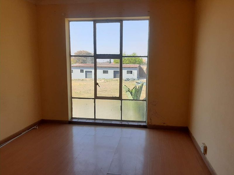 An empty bedroom featuring laminate flooring and a large metal-framed window providing natural light and exterior views.