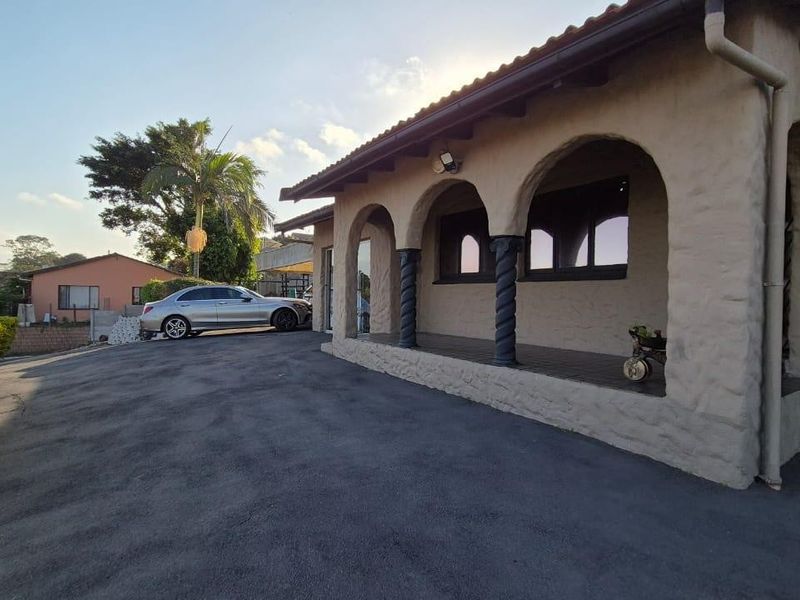 Front view of the house featuring a covered veranda with arched openings, textured exterior walls, and a paved driveway.