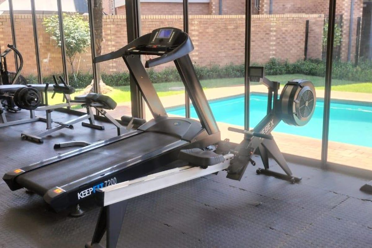 A well-lit gym featuring rubberized flooring and floor-to-ceiling glass walls that provide a direct view of the outdoor swimming pool area.