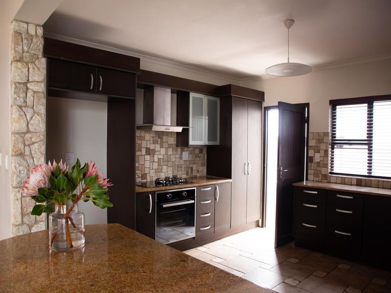 Modern kitchen featuring dark wood cabinetry, granite countertops, stone tile backsplash, and a stone feature pillar, with integrated oven and gas hob.