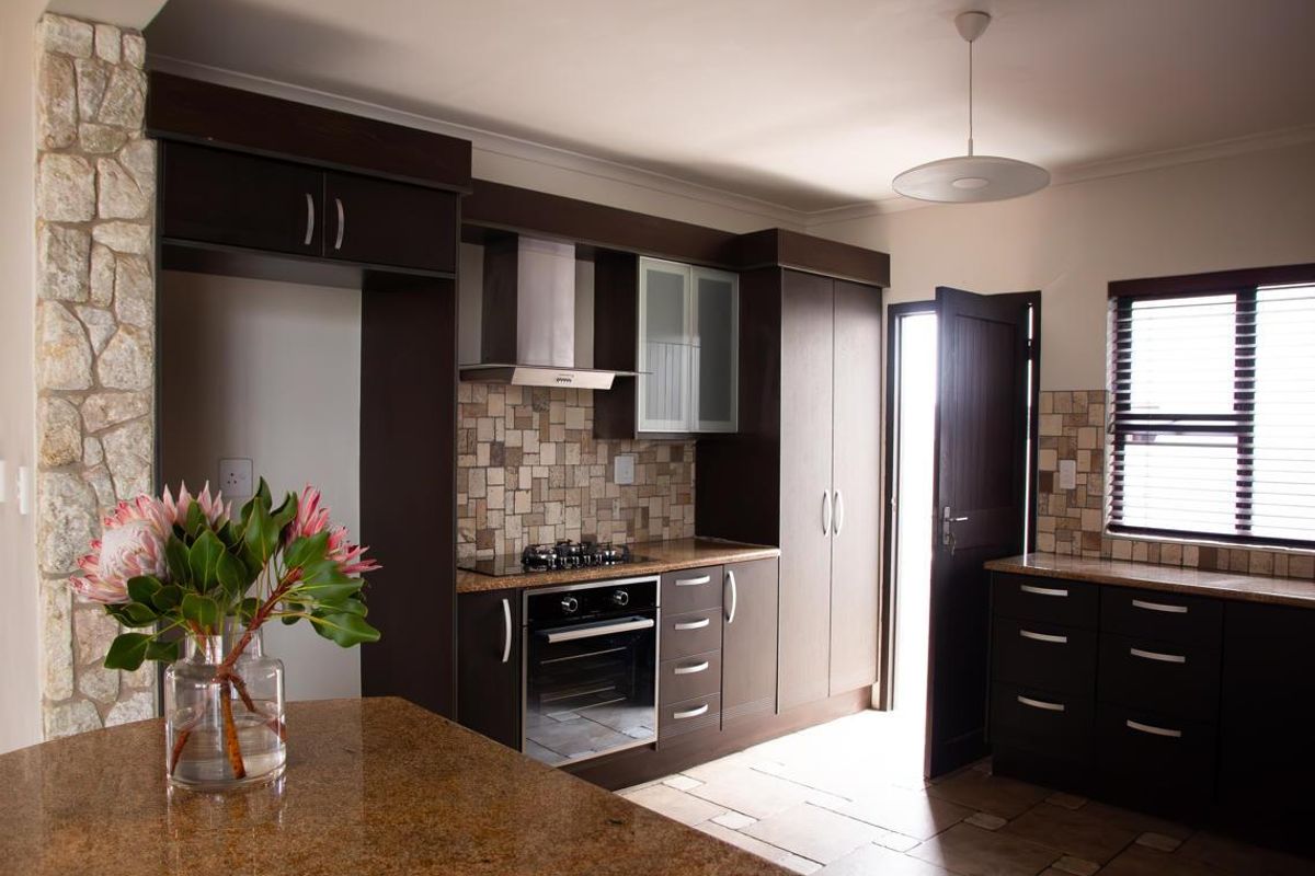 Modern kitchen featuring dark wood cabinetry, granite countertops, stone tile backsplash, and a stone feature pillar, with integrated oven and gas hob.