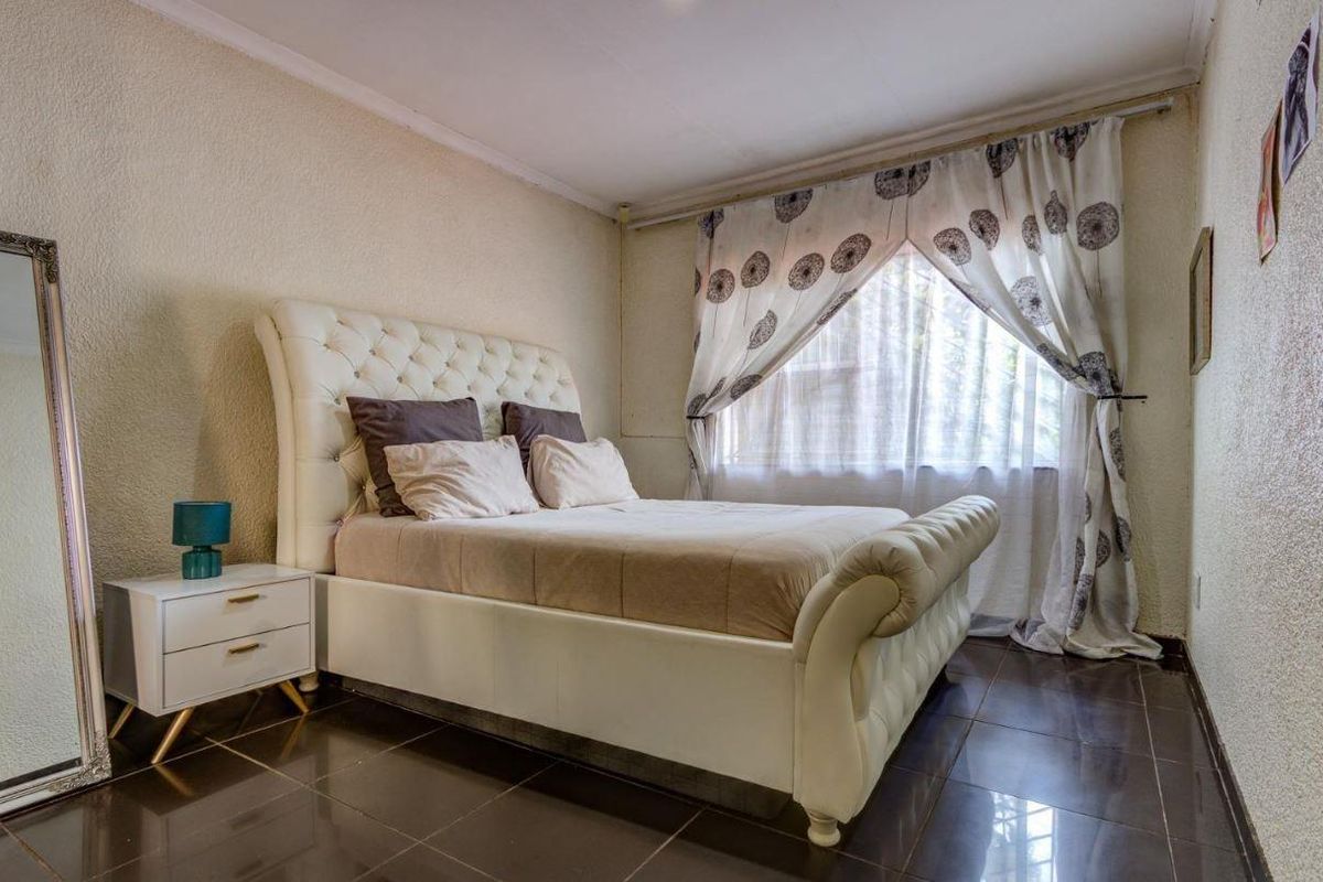 A bedroom featuring dark tiled flooring and a window with a curtain rail.
