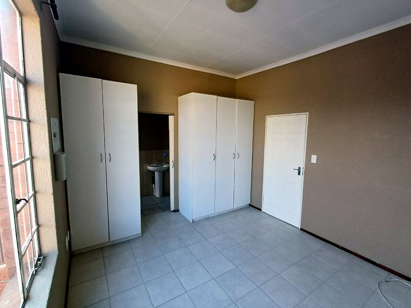A spacious, empty bedroom featuring neutral tiled flooring, built-in cupboards, and direct access to an en-suite bathroom.