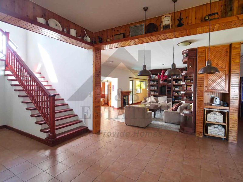 Spacious open-plan living area featuring a prominent wooden staircase, tiled floors, and integrated cabinetry, creating a warm and traditional aesthetic.