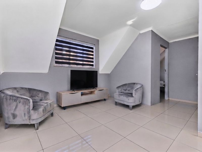A modern living area featuring neutral grey walls, tiled flooring, and a sloped ceiling design with natural light from a window with roller blinds.
