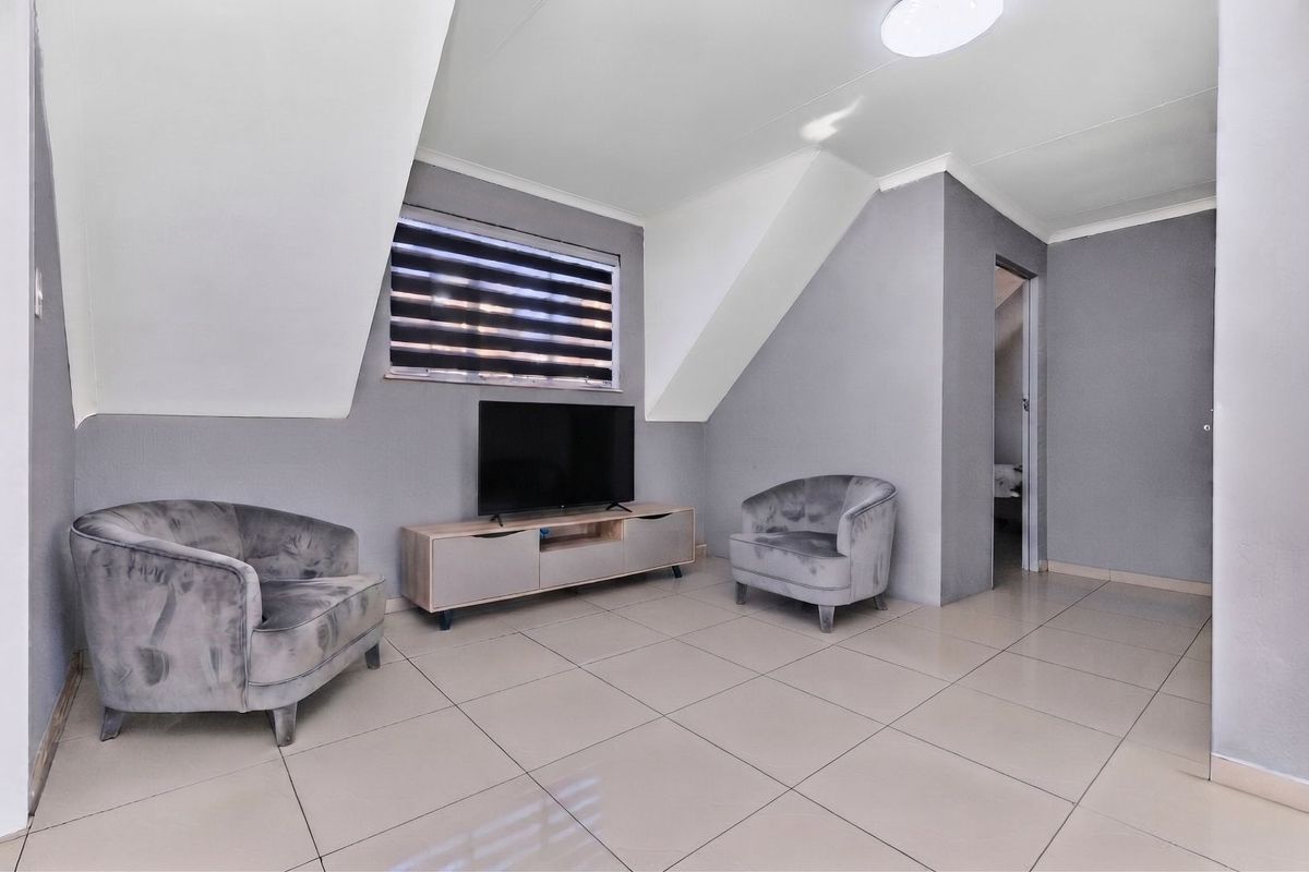 A modern living area featuring neutral grey walls, tiled flooring, and a sloped ceiling design with natural light from a window with roller blinds.