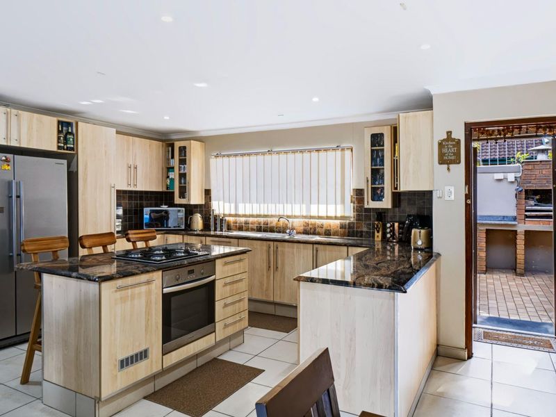 Functional kitchen featuring light wood cabinetry, dark granite countertops, built-in oven, gas cooktop, and direct access to an outdoor patio area.