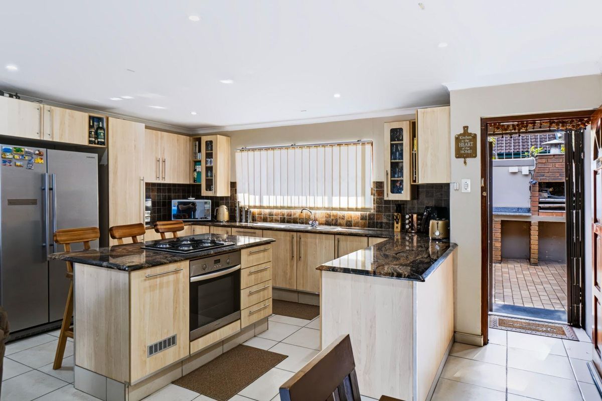 Functional kitchen featuring light wood cabinetry, dark granite countertops, built-in oven, gas cooktop, and direct access to an outdoor patio area.
