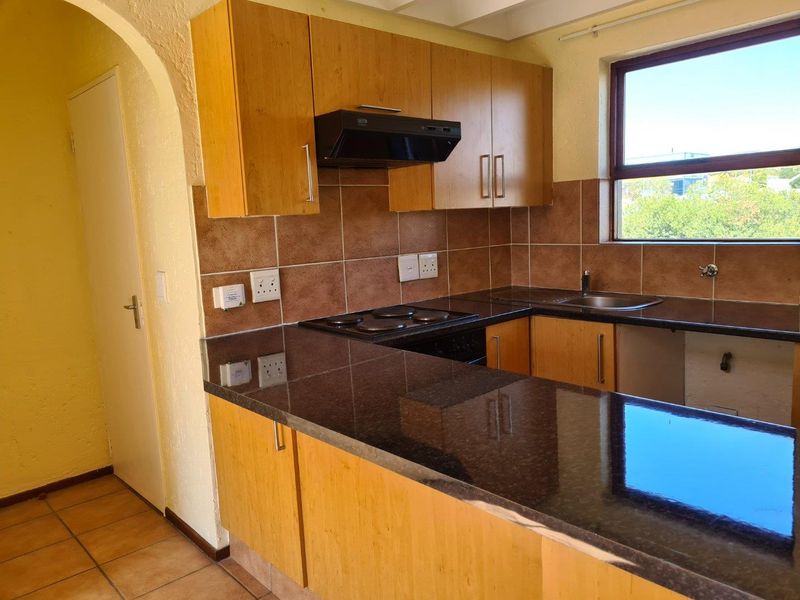 A functional kitchen featuring wood-finish cabinetry, dark granite countertops, a built-in electric hob with extractor, and tiled backsplash.