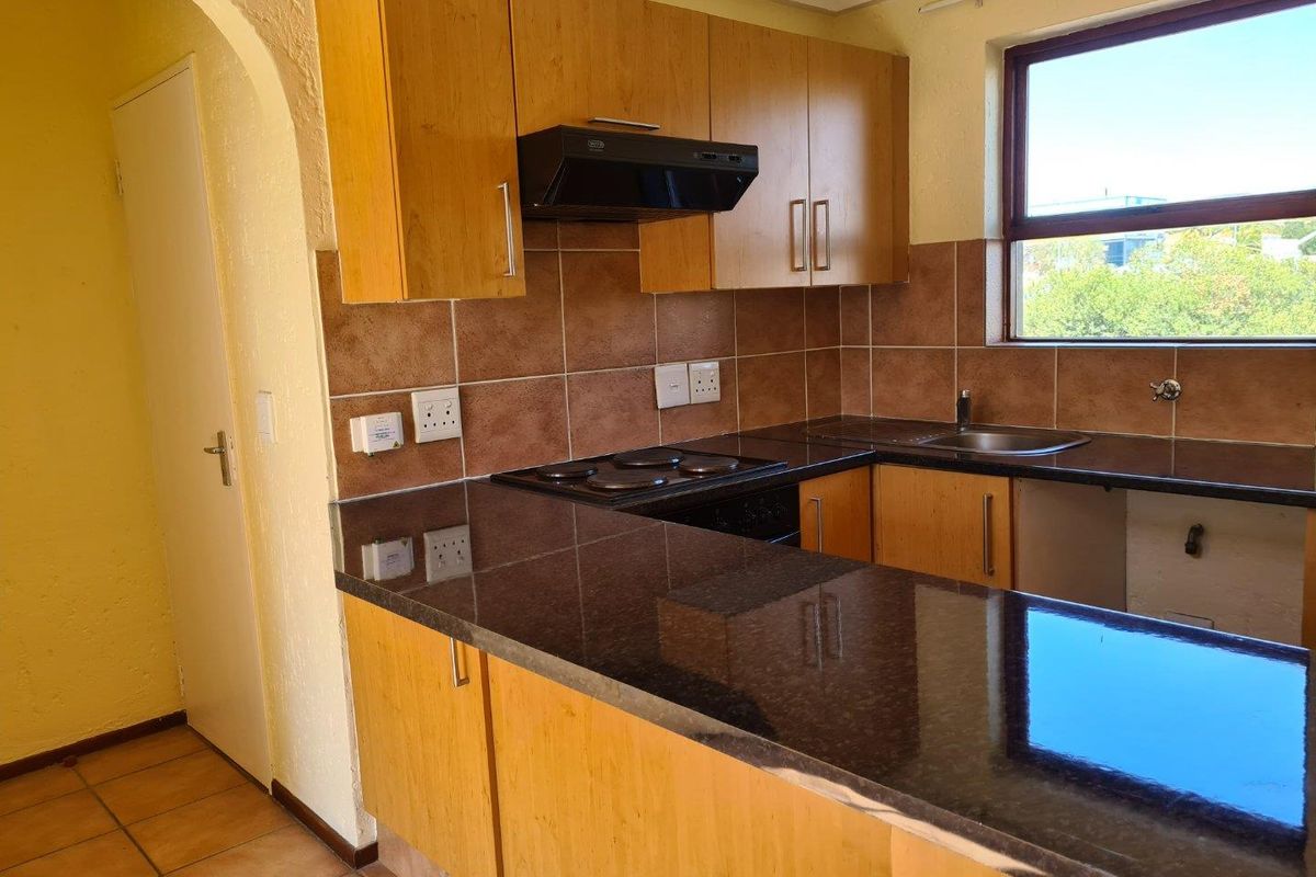 A functional kitchen featuring wood-finish cabinetry, dark granite countertops, a built-in electric hob with extractor, and tiled backsplash.