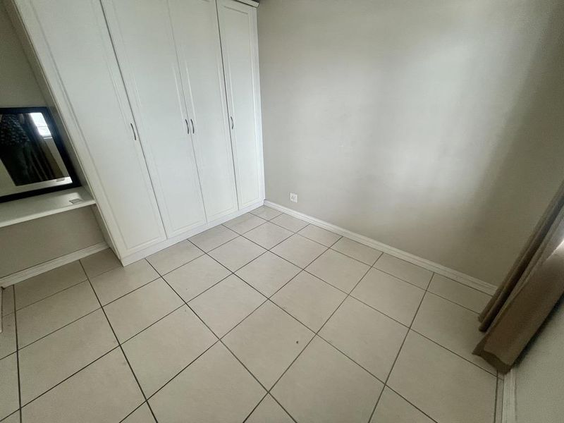 A clean, empty bedroom featuring neutral tiled flooring and a white built-in wardrobe with integrated shelving.