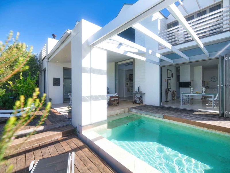 Outdoor pool area featuring a timber deck, covered patio with bi-fold doors, and a pergola, creating a seamless transition between indoor and outdoor living spaces.