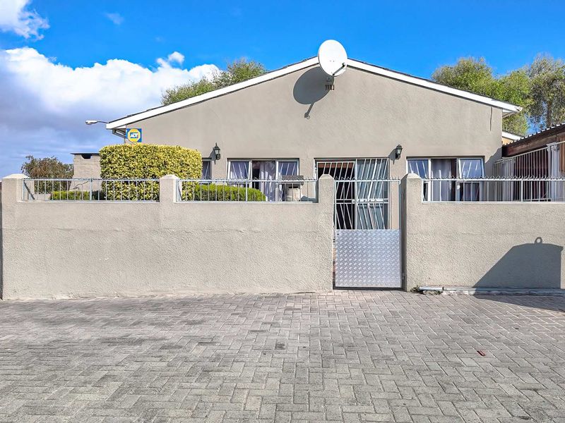 Front view of the property featuring a paved driveway, secure perimeter wall with metal gate, and exterior security lighting.