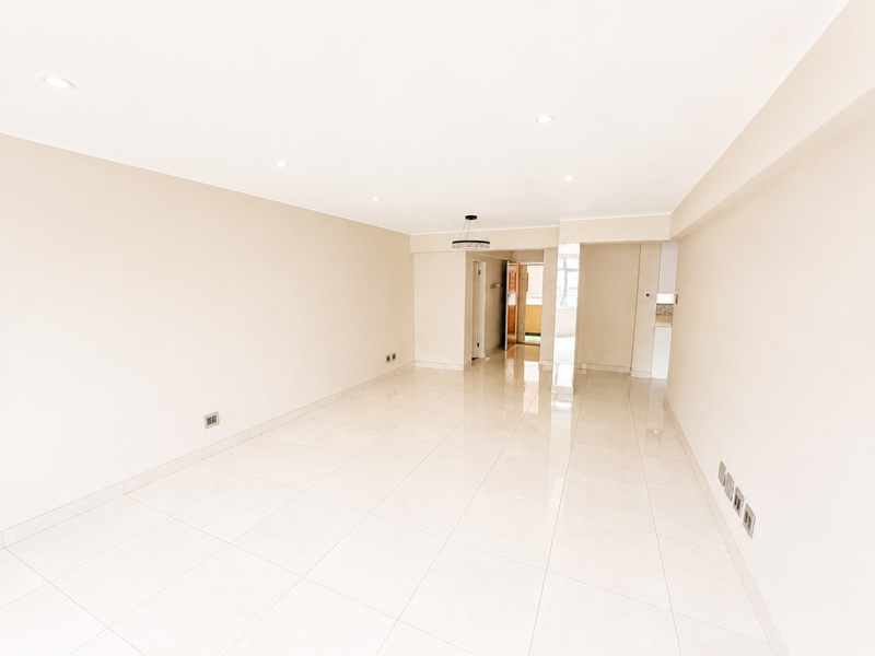 A bright, spacious, and empty living area featuring neutral walls, polished porcelain floor tiles, and modern recessed downlighting throughout.