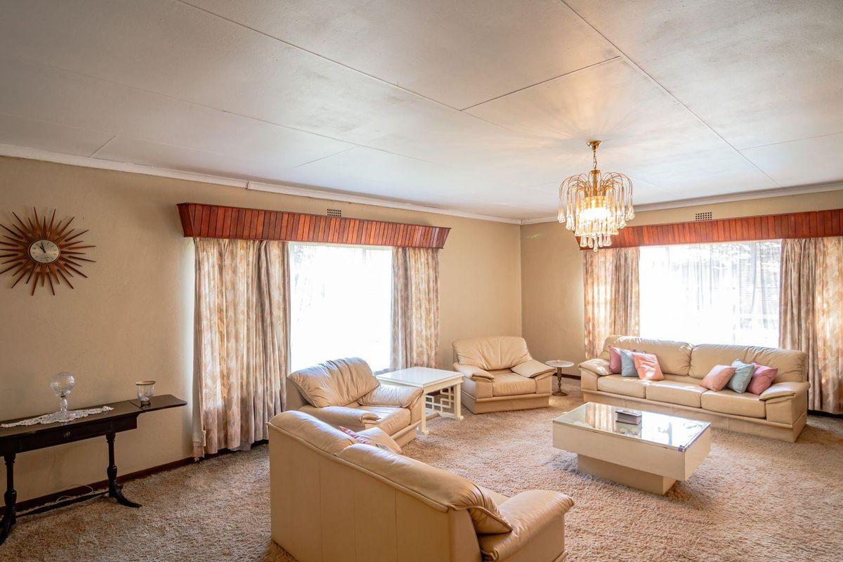 Spacious living room featuring large windows with wooden pelmets, neutral wall finishes, and a classic chandelier, offering a comfortable and traditional living space.
