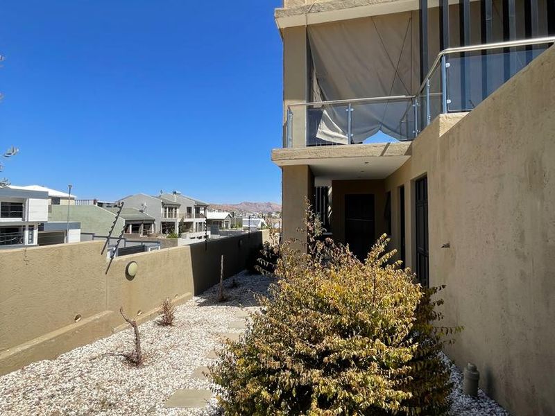Rear exterior view featuring a gravel garden, stone pathway, and an upper-level balcony with a glass balustrade and privacy screen.