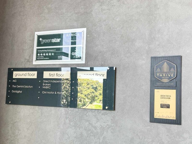 A professional building directory and certification display mounted on a textured grey wall, showcasing tenant locations and sustainability credentials.