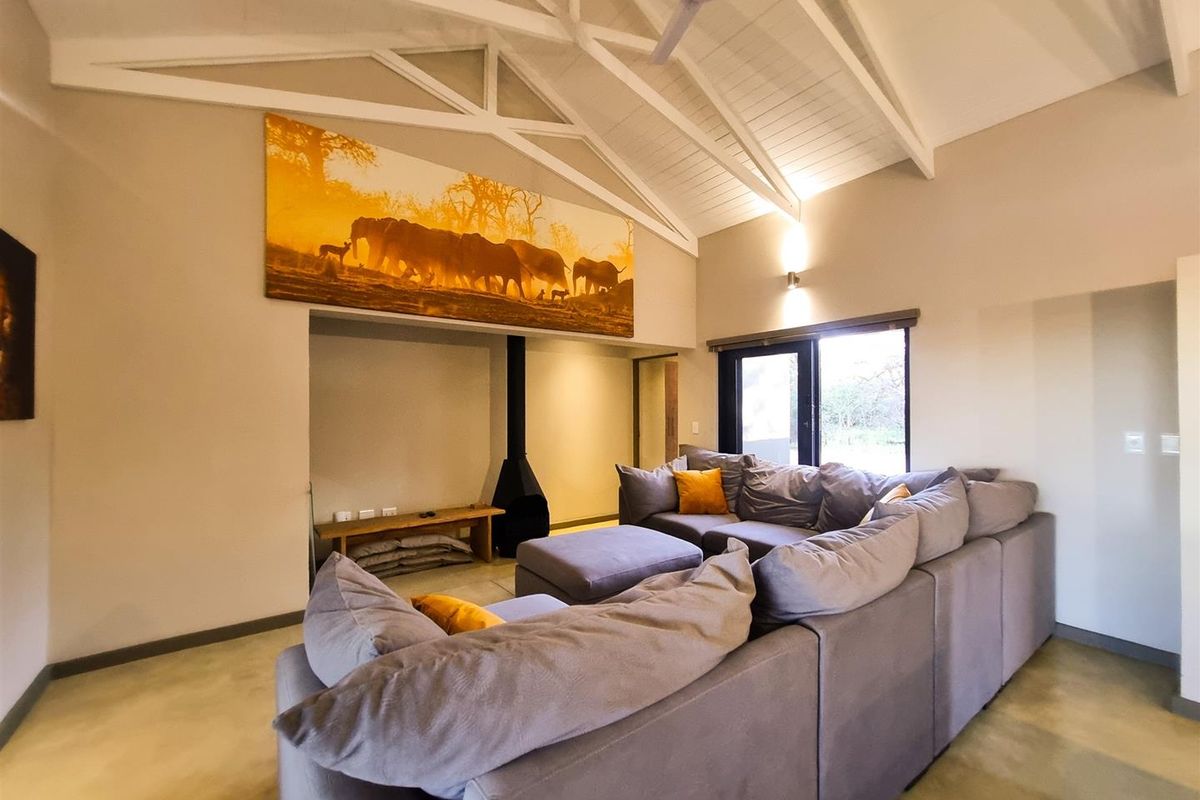 Spacious living room featuring a high vaulted ceiling with exposed trusses, a modern freestanding fireplace, and large glass doors leading to the outdoors.