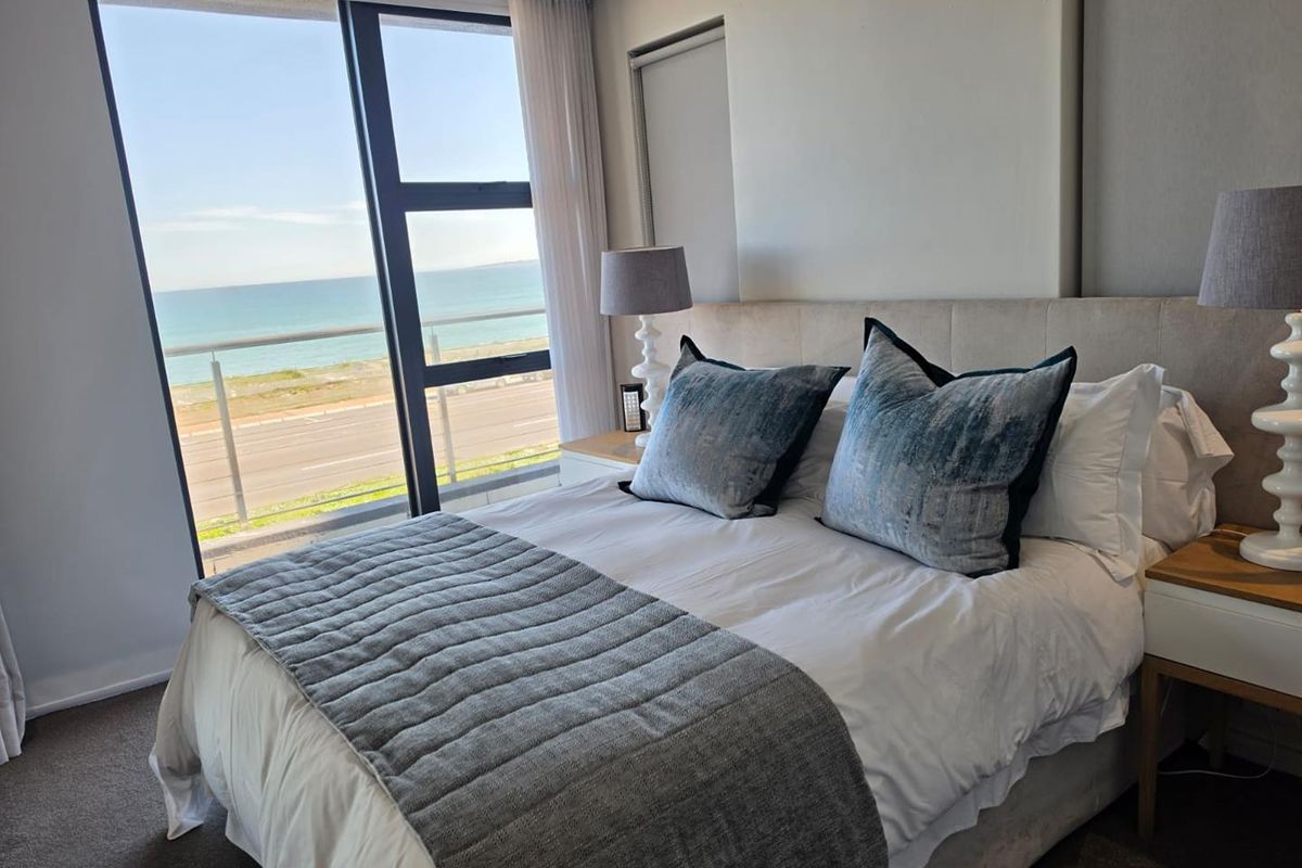 Modern bedroom featuring floor-to-ceiling windows with direct access to a balcony and expansive ocean views.