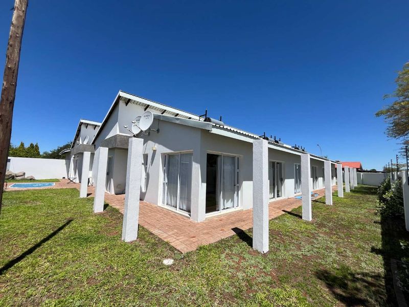 Rear view of the guest house featuring a paved patio area, sliding glass doors, and well-maintained exterior walls with solar water heating infrastructure.