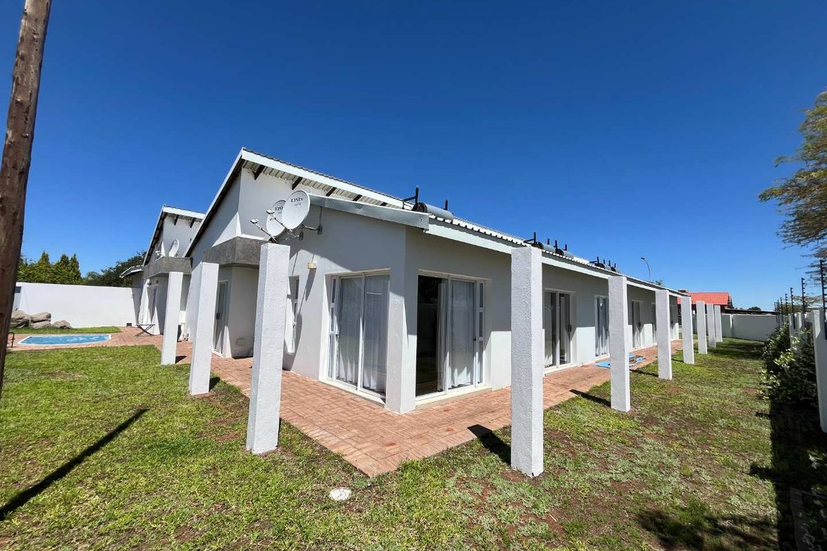 Rear view of the guest house featuring a paved patio area, sliding glass doors, and well-maintained exterior walls with solar water heating infrastructure.