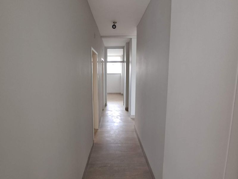 A clean, neutral-toned hallway featuring tiled flooring and recessed lighting, providing a bright and functional transition space within the apartment.