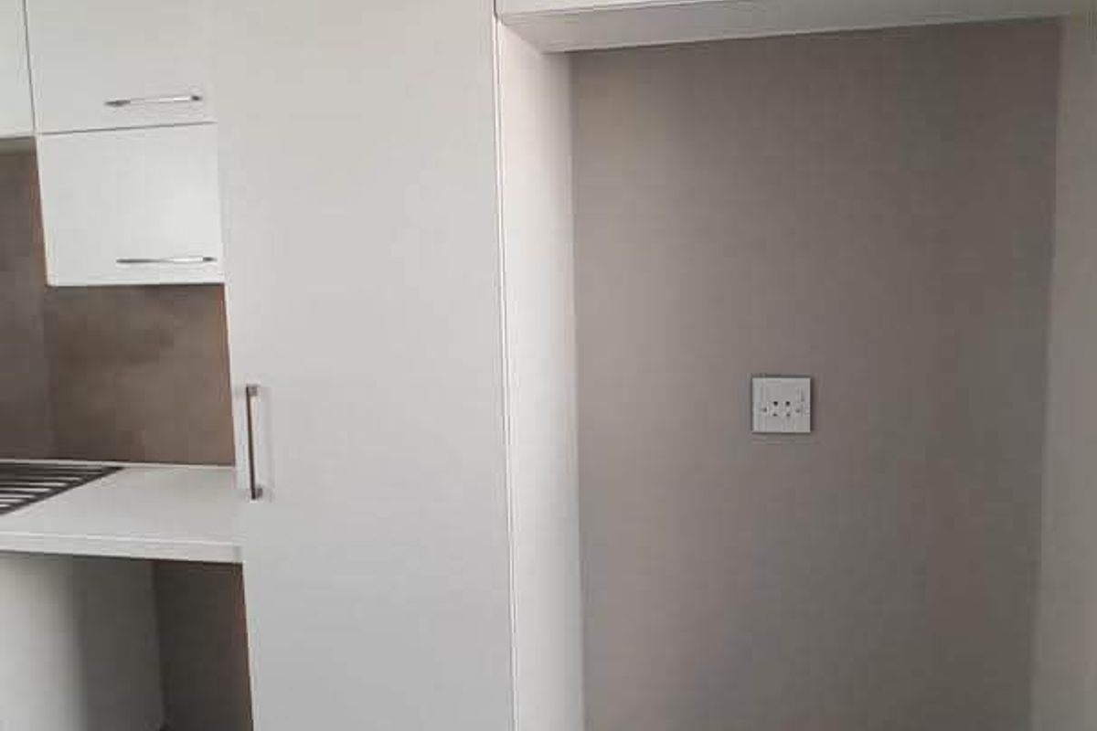 A clean, modern kitchen area featuring white built-in cabinetry, neutral wall tones, and tiled flooring with a dedicated space for a refrigerator.