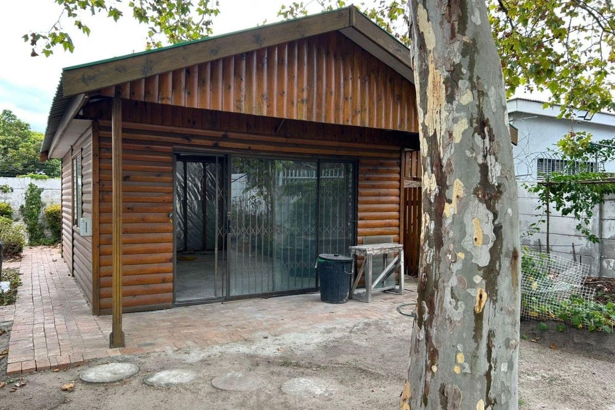 A detached log cabin style structure featuring a pitched roof, sliding glass doors with security gates, and an adjacent brick paved patio area.