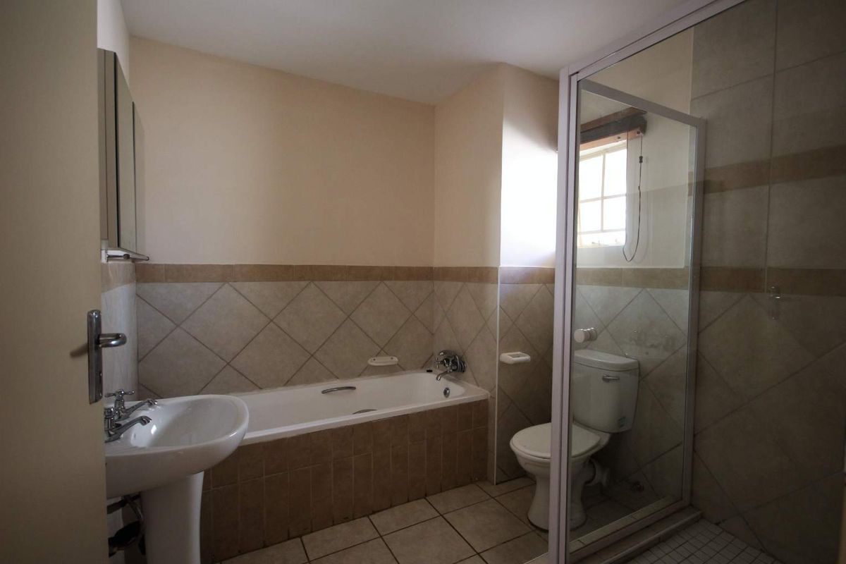 A functional bathroom featuring a pedestal basin, built-in bathtub, separate shower enclosure, and toilet with neutral tiled finishes.