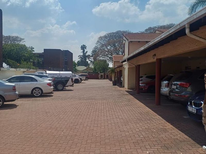 An outdoor parking area featuring a paved driveway and covered parking bays with structural support pillars.