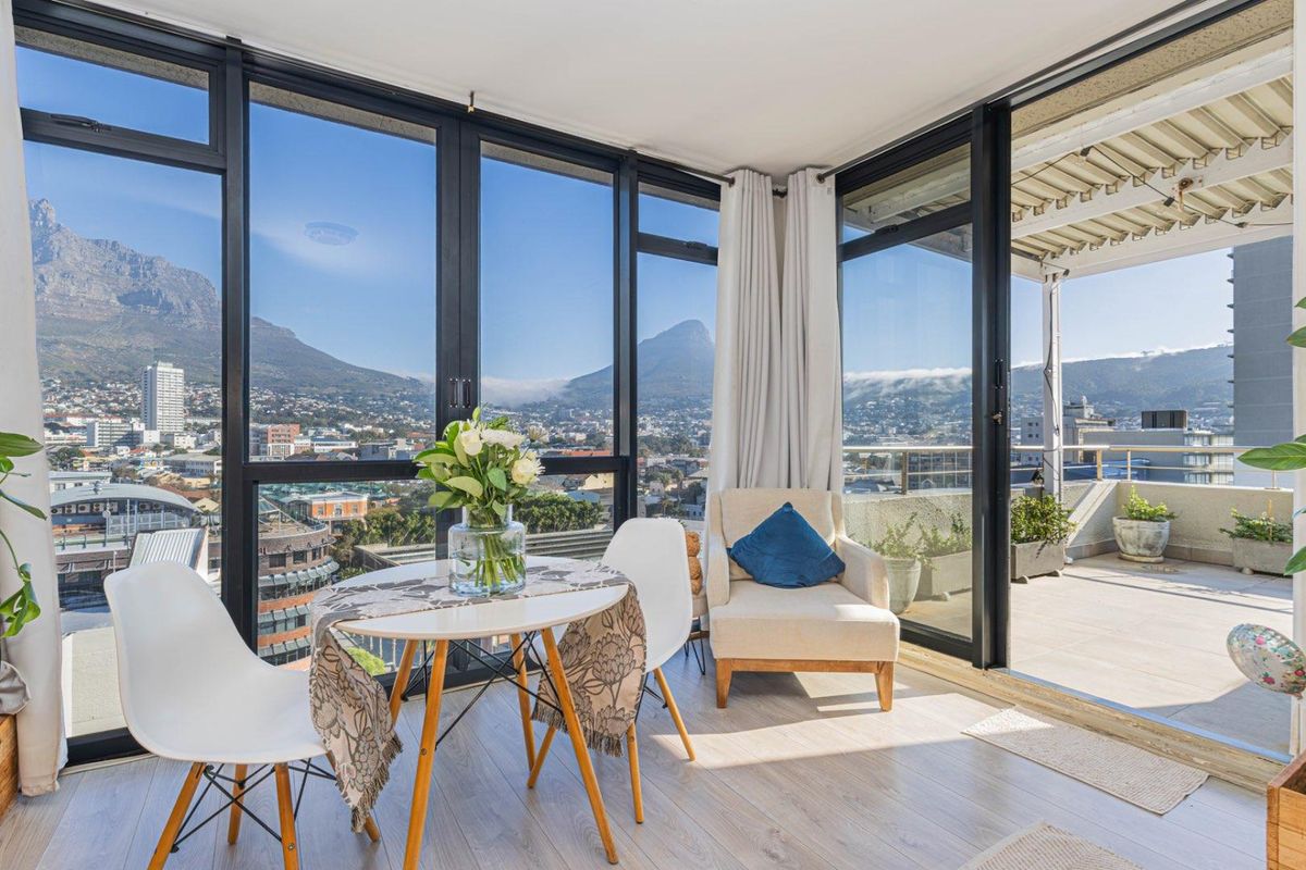 Bright sunroom featuring floor-to-ceiling windows with panoramic mountain and city views, seamlessly connecting to an outdoor balcony area.