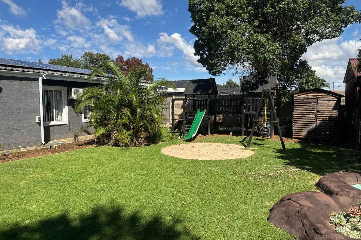 A well-maintained rear garden featuring a manicured lawn, circular paved area, and established landscaping adjacent to the house exterior.