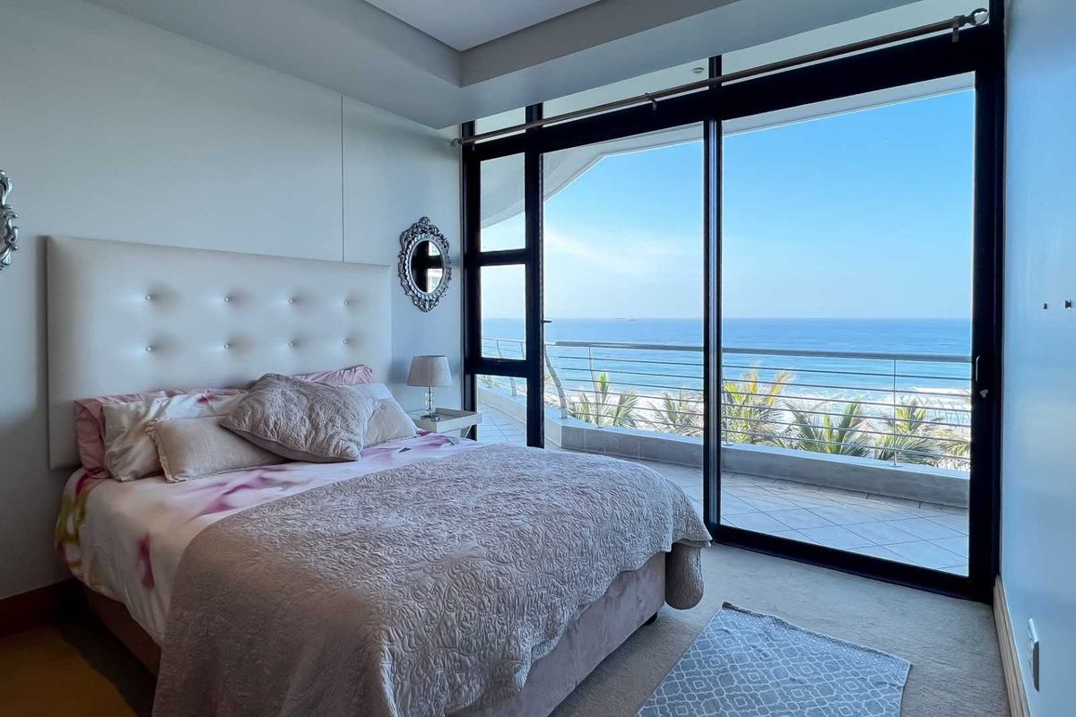 Bright bedroom featuring floor-to-ceiling sliding glass doors that open onto a private balcony with expansive ocean views.