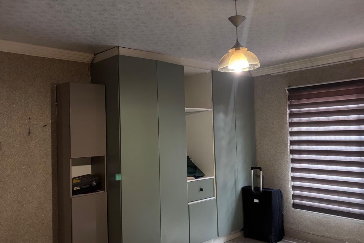 Bedroom featuring built-in wardrobes, ceiling pendant lighting, and roller blinds. The room requires cosmetic updates to the wall finishes.