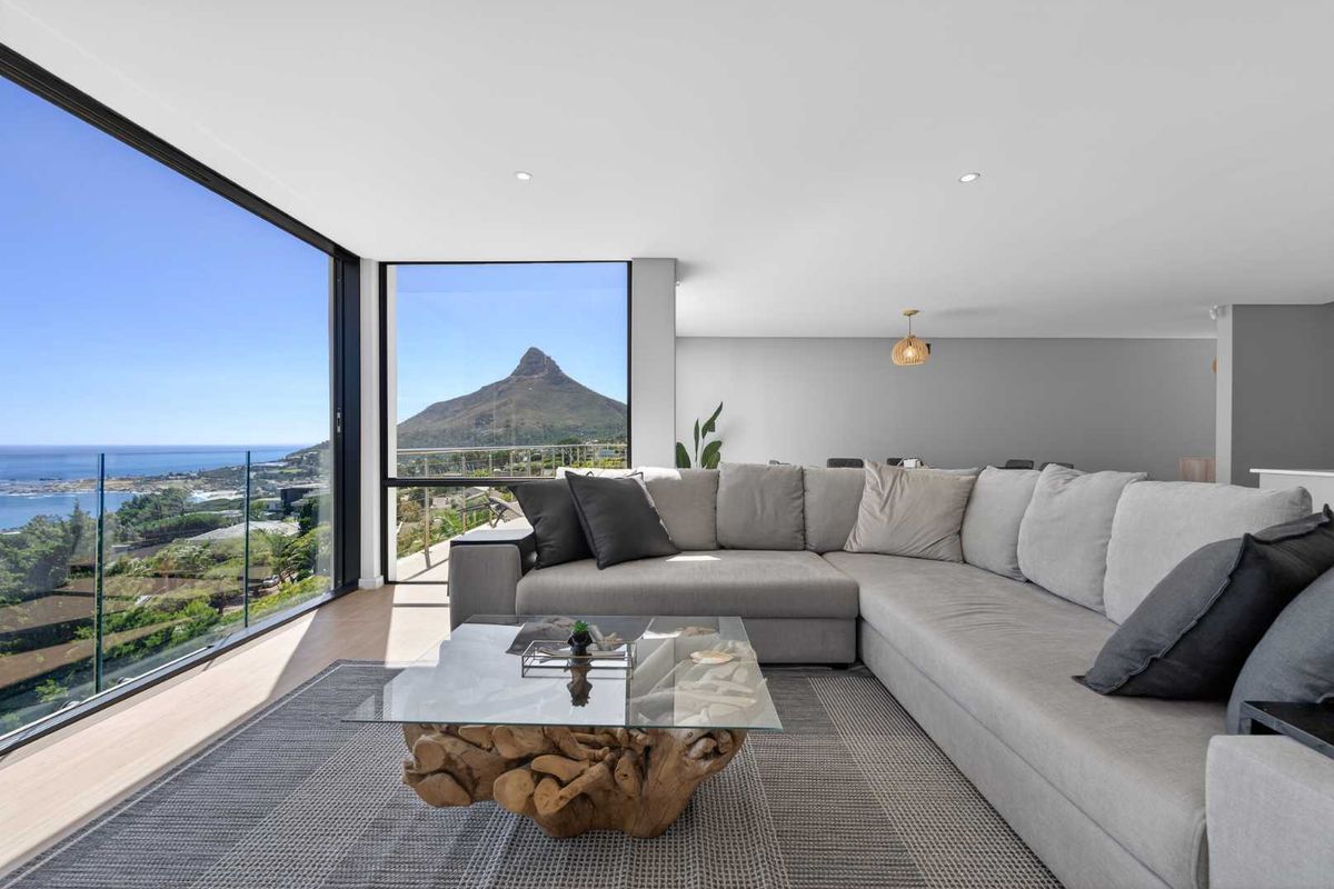 Modern living room featuring expansive floor-to-ceiling windows with panoramic mountain and ocean views, recessed lighting, and high-quality hardwood flooring.