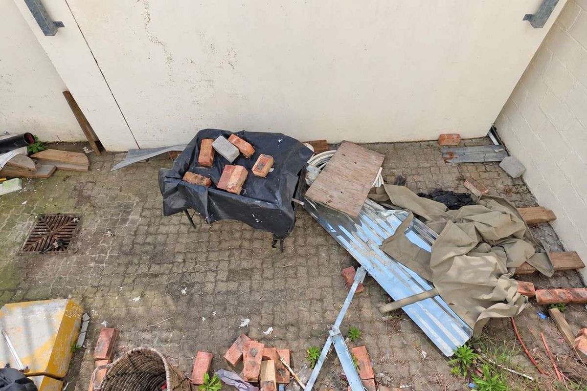 An exterior rear area featuring paved ground and masonry walls, currently used for storage with significant debris and clutter present.