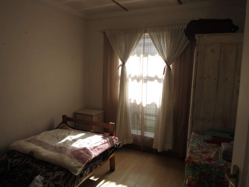 A bedroom featuring laminate flooring and a window with curtains, providing natural light to the space.