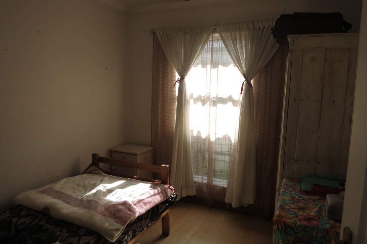 A bedroom featuring laminate flooring and a window with curtains, providing natural light to the space.