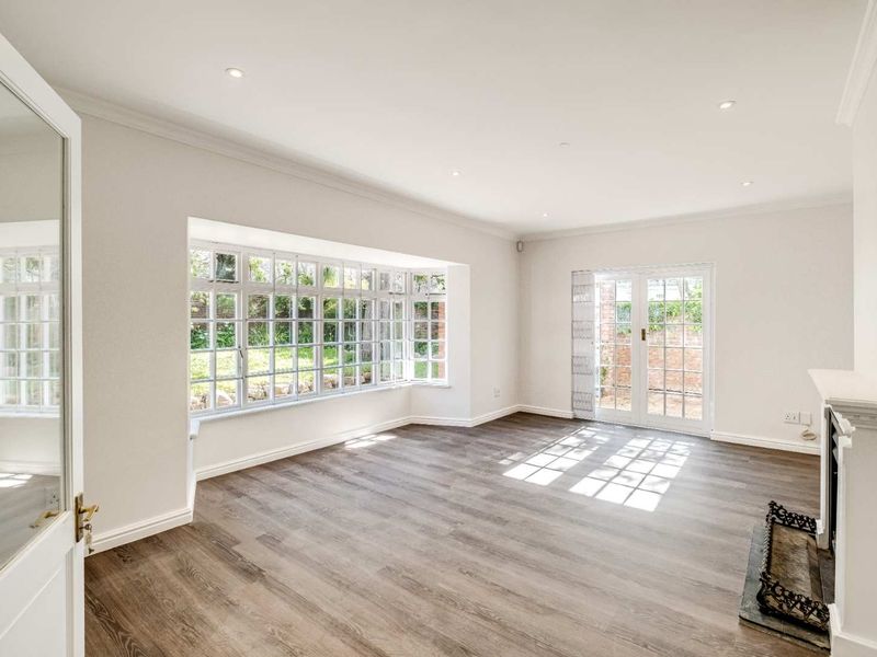 Bright and spacious living room featuring a large bay window, fireplace, and french doors leading to the garden, finished with modern laminate flooring.