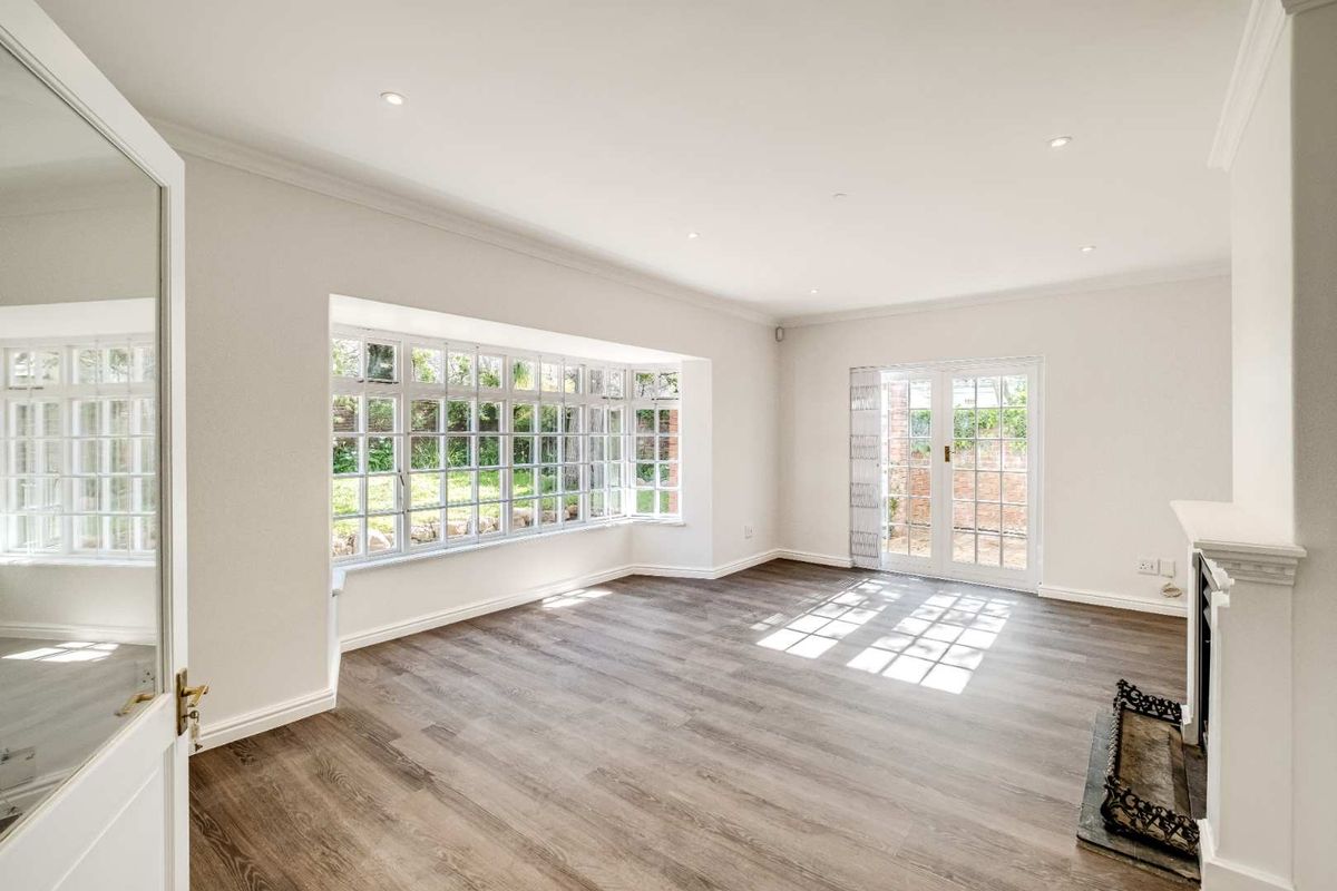 Bright and spacious living room featuring a large bay window, fireplace, and french doors leading to the garden, finished with modern laminate flooring.