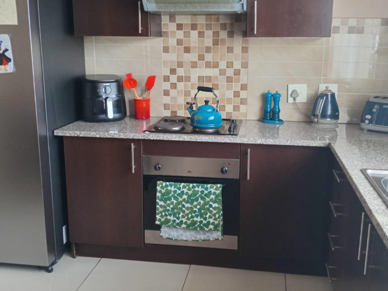 A functional kitchen featuring dark laminate cabinetry, granite countertops, a tiled backsplash, and integrated cooking appliances including an oven and extractor fan.